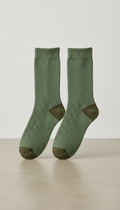 A pair of Leaf Green cotton socks centered on a simple, textured neutral surface. The background is clean and minimal,...